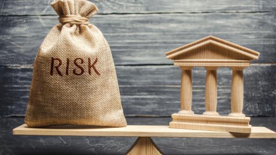 A money bag with the word Risk and a bank building on the scales