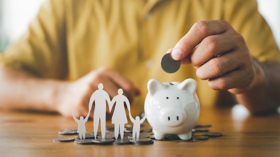  Person putting coin in piggybank next to paper cut-out family 