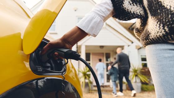 Woman plugging electric charger into car outside Home With Family